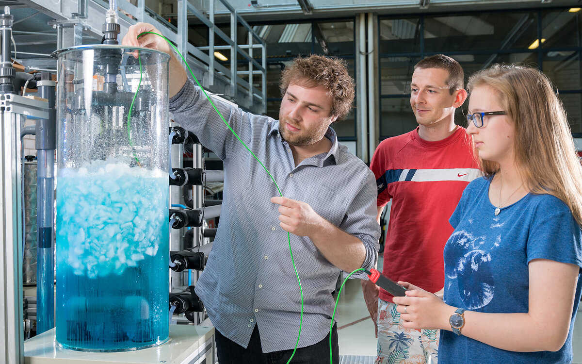 three students at the lab putting a probe into a glass cylinder containing ice slurry