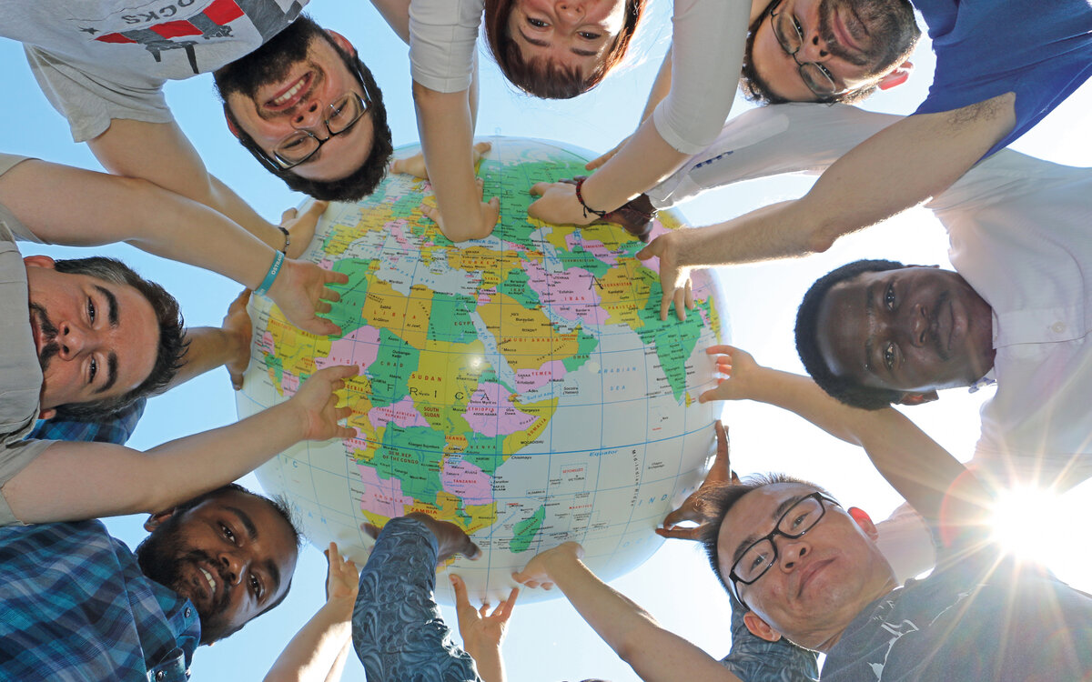 students in a circle lifting a globe over their heads, seen from ground level