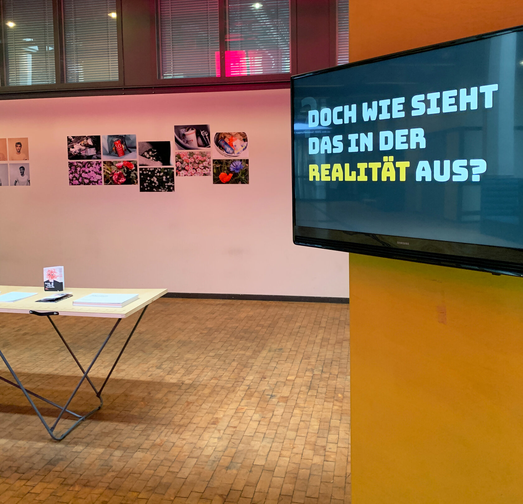 Ausstellung im Foyer des ZKM: Fotografien, ein Tisch mit Fotobüchern sowie ein großer Bildschirm mit der Frage "Doch wie sieht es in der Realität aus?"