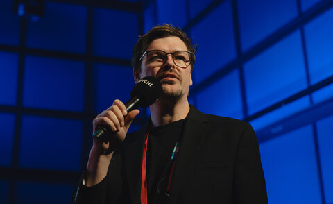 Daniel Hepperle stands on a stage with a microphone.